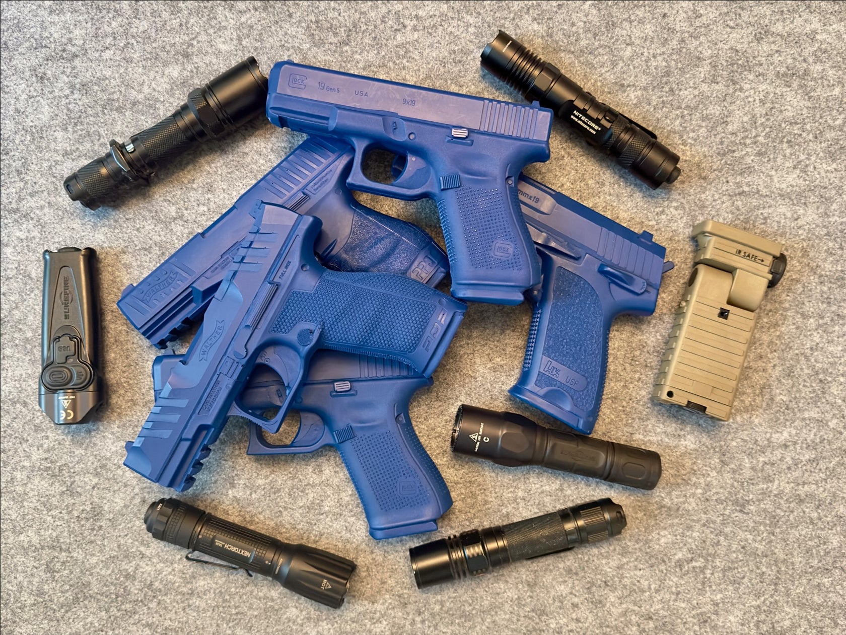 Taschenlampen und Pistolen Attrappen sind auf einem grauen untergrund drapiert.