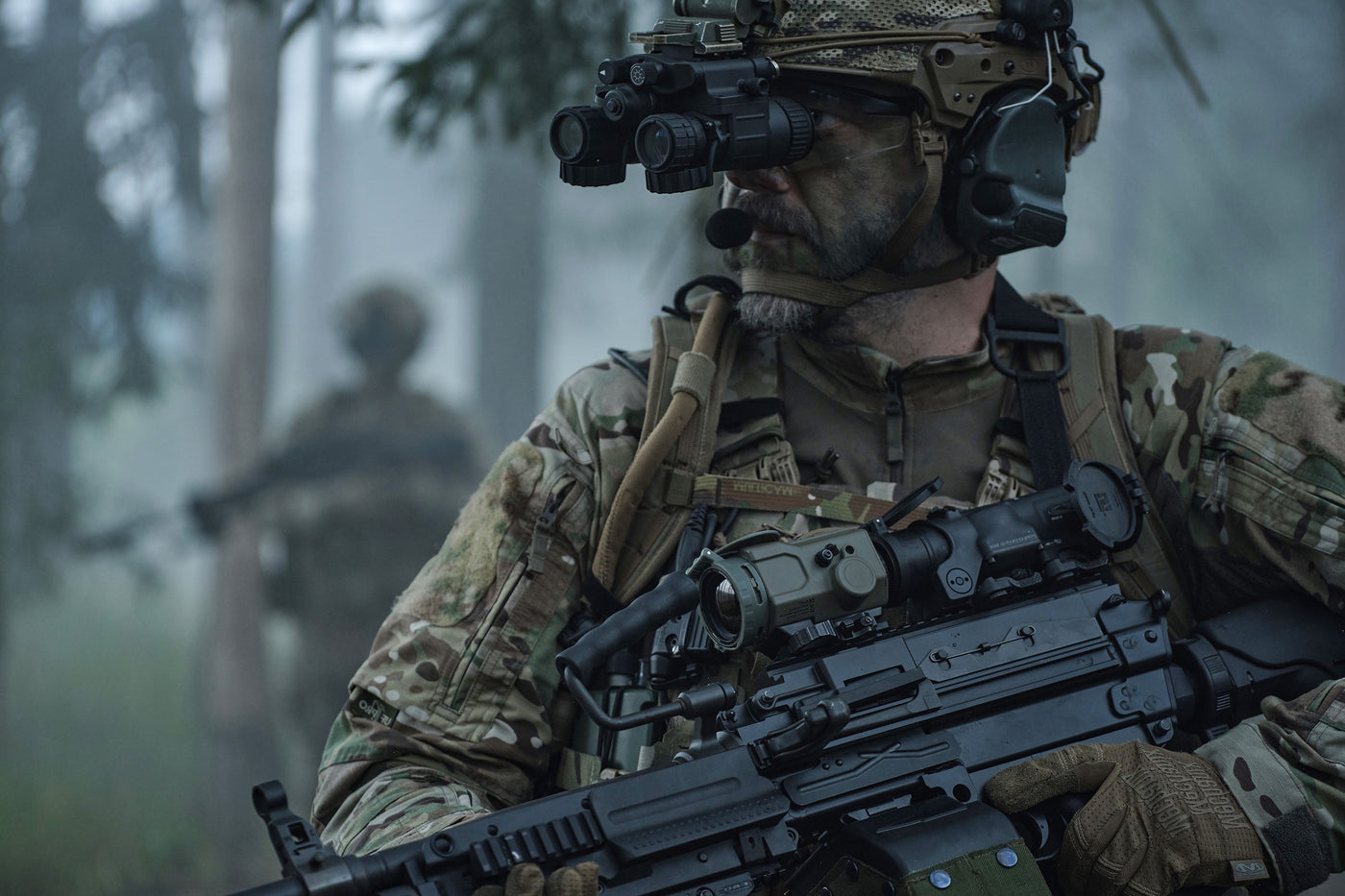 Ein Soldat steht in einem nebligem Wald. Auf seiner FN Minimi ist ein PumIR mit vor einem ELCAN befestigt
