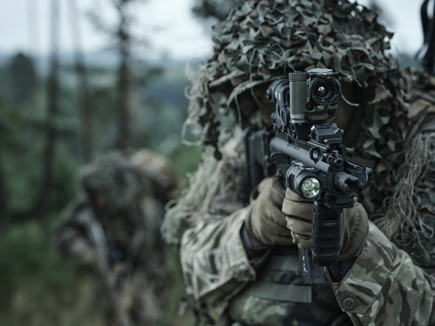 Ein Soldat im Wald zielt mit einer TILO auf einem Sturmgewehr