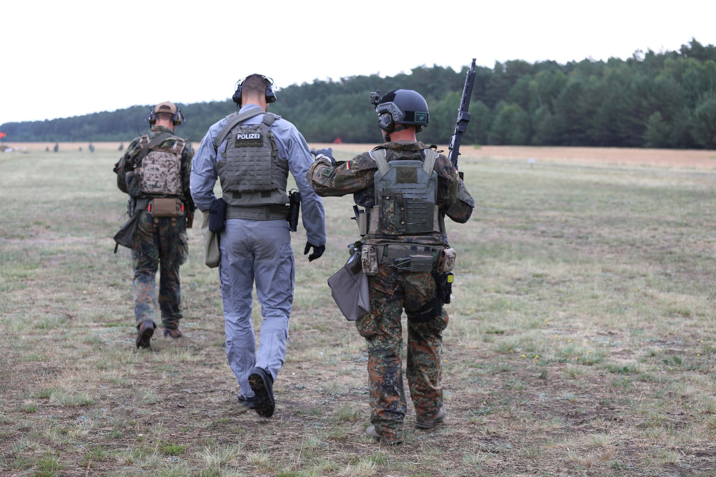 Zwei Soldaten und ein Polizist gehen weg, der Kamera mit dem Rücken zugewandt.
